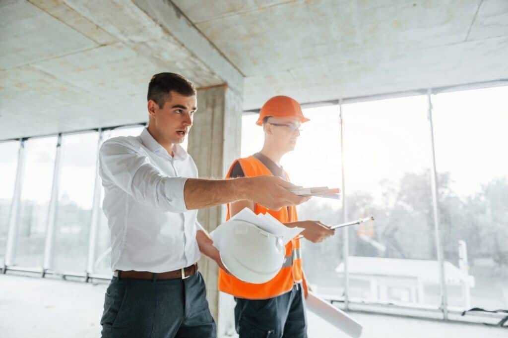 Planning the process. Man in suit and handyman in orange protective wear is working on construction